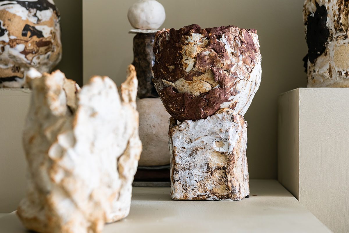 Rough, textured ceramic vessels in white, rust and black clay displayed on pale shelves